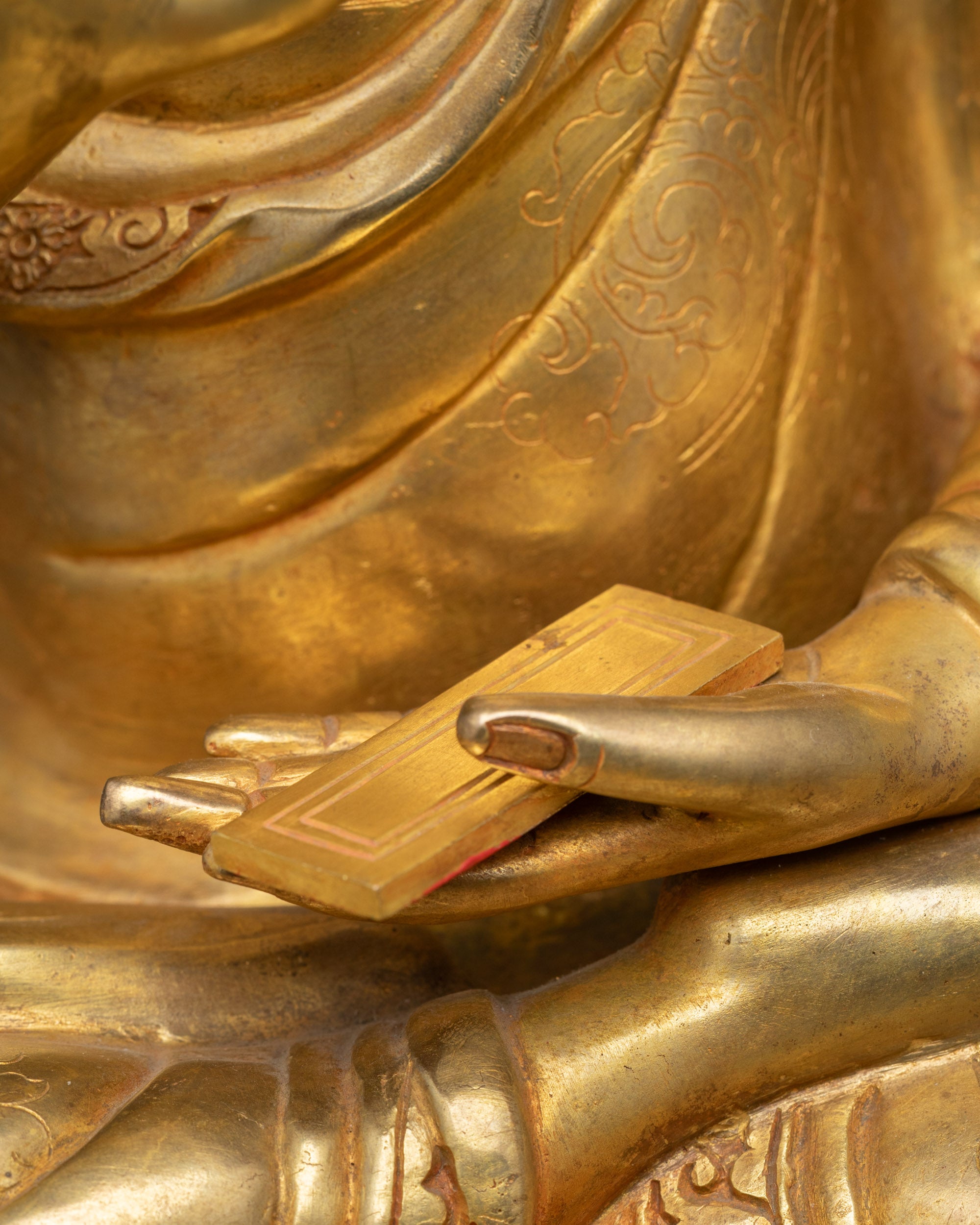 Side view of Tsongkhapa statue with fire-gilded copper body and fine detailing of robes.