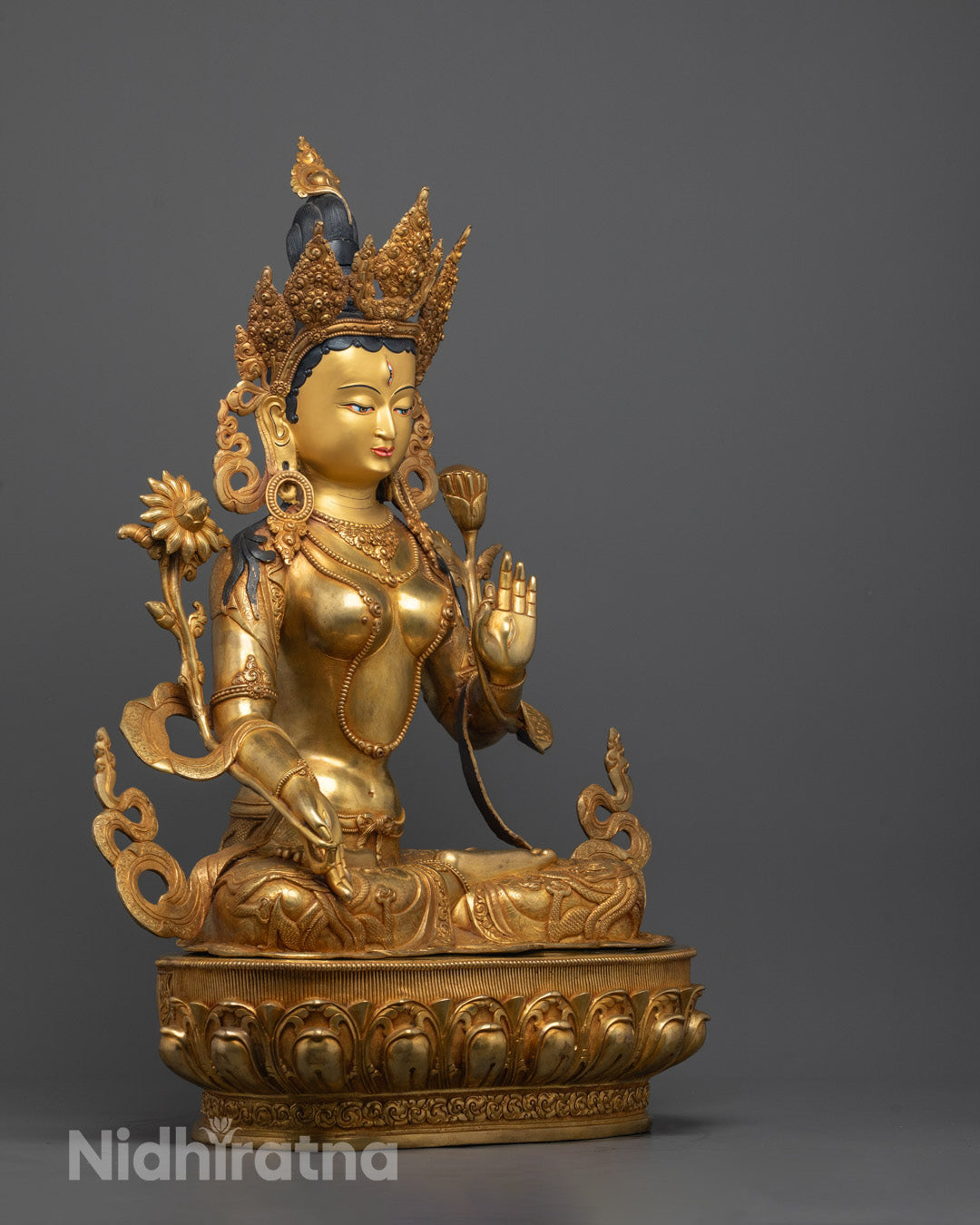 Side view of White Tara statue, fire-gilded body, blessing mudra. Detailed carvings.