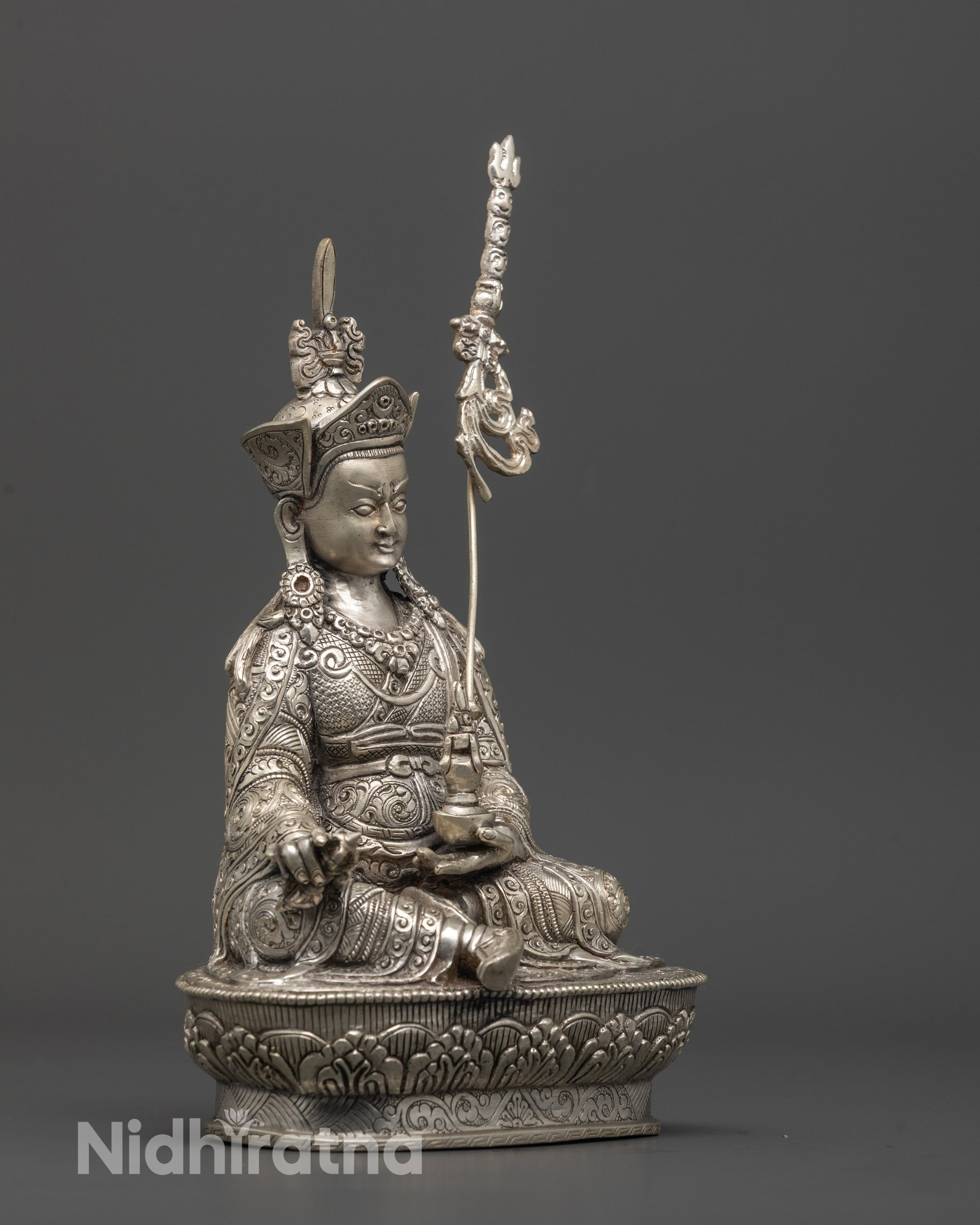 Side view of intricately detailed silver-plated Guru Rinpoche statue on copper base