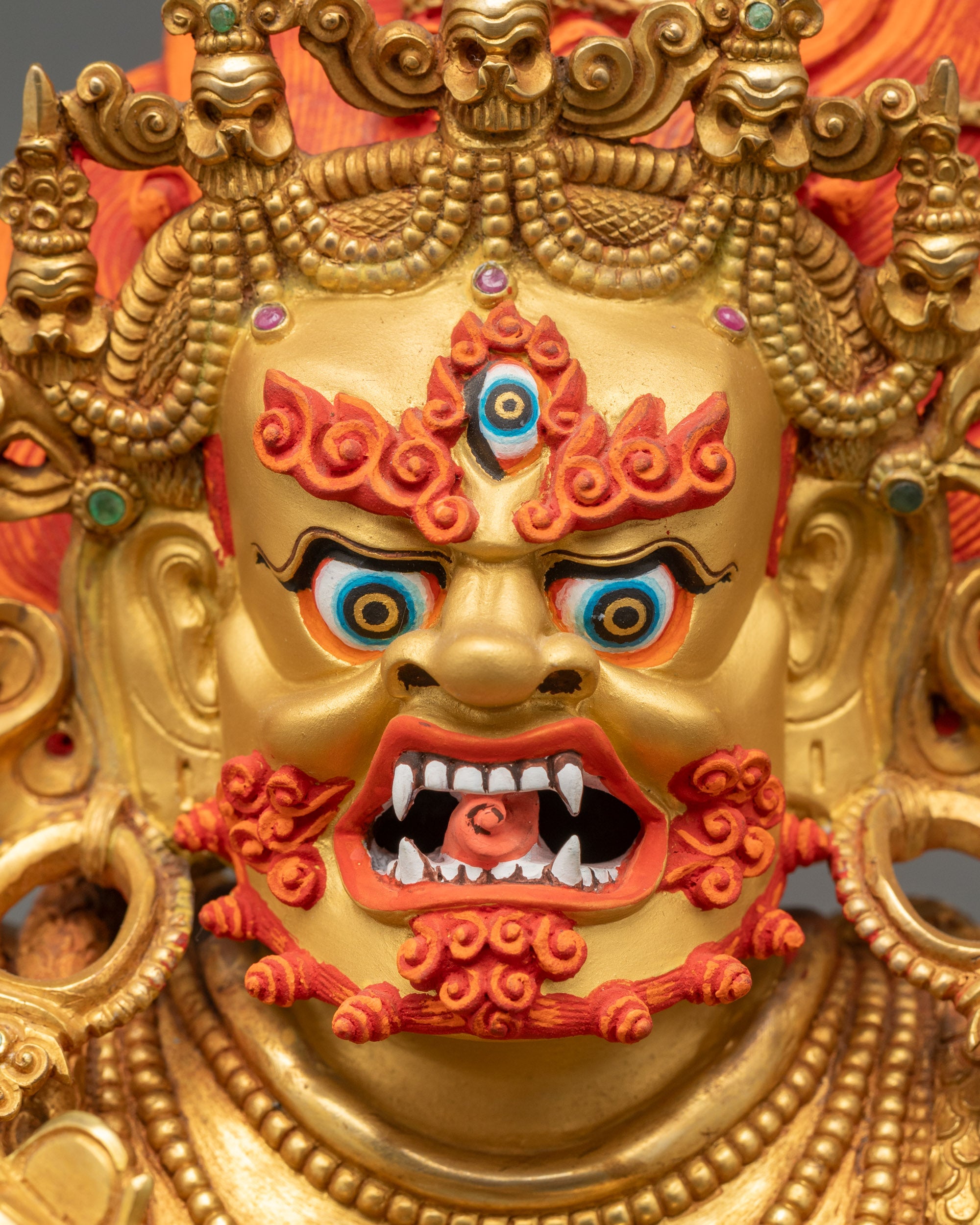 Detailed close-up of Mahakala’s fierce gold-gilded face, third eye, bared fangs, red eyebrows, and flowing beard