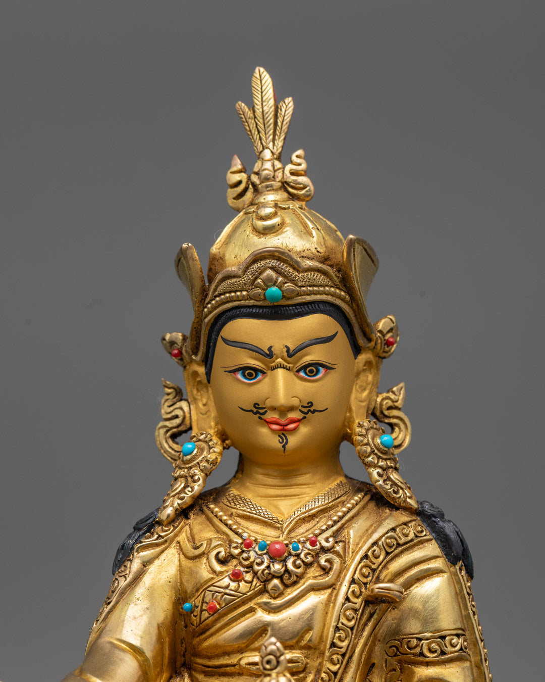 Vivid acrylic colors and semi-precious stones decorate the Guru Rinpoche statue, featuring detailed carvings on the khata scarf and traditional monastic robes.