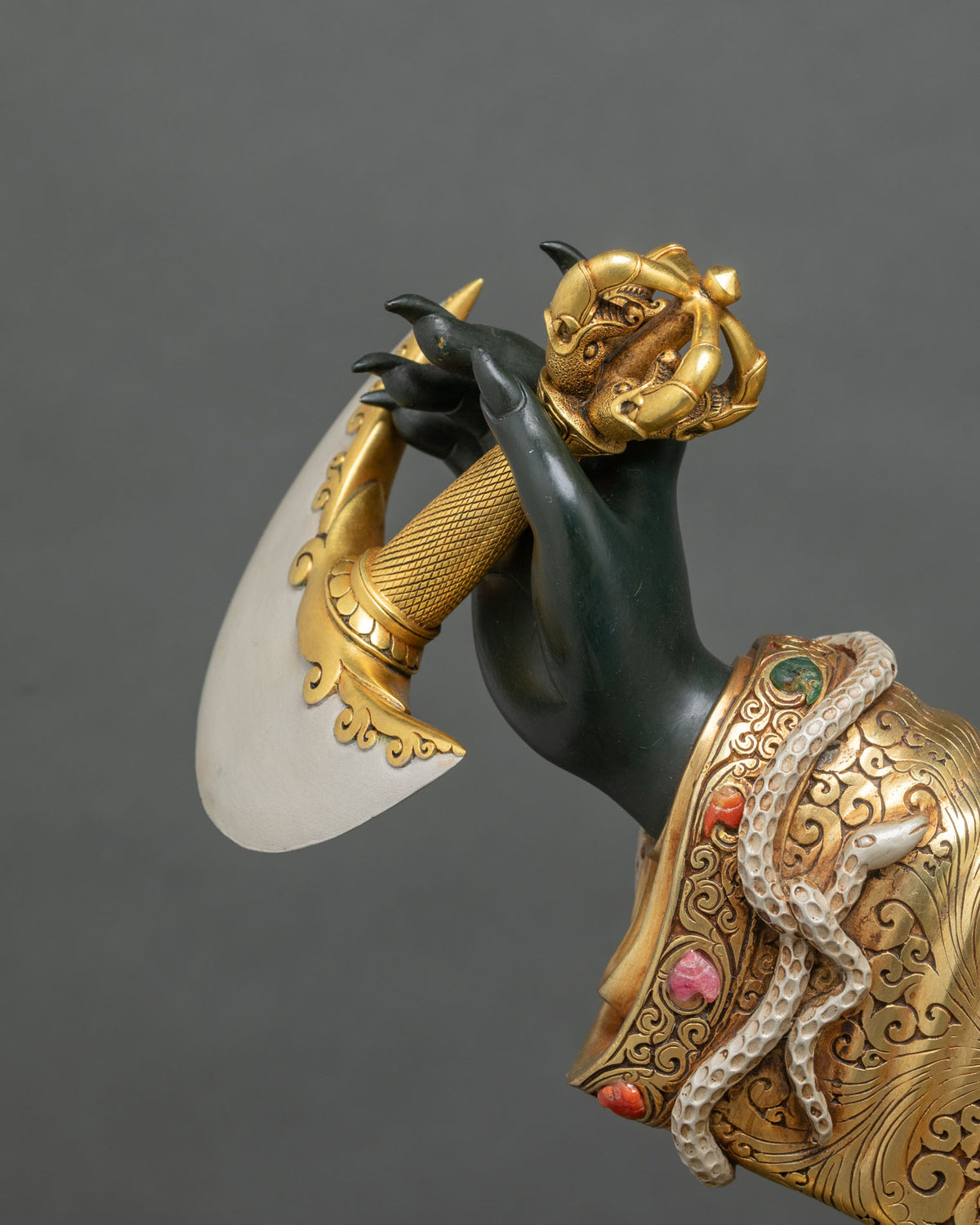 Raised hand of Mahakala Bernagchen holding the kartika knife with gold vajra handle and crescent blade