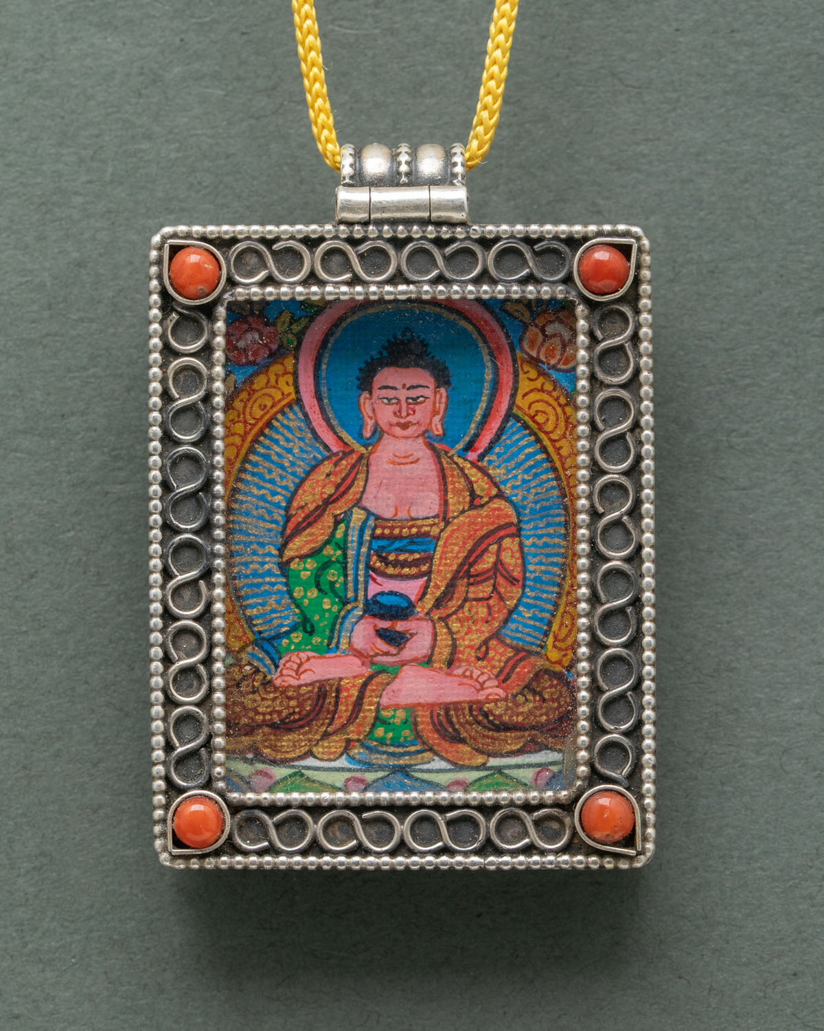 Amitabha Buddha locket made from silver with intricate floral filigree and semi-precious coral stones.