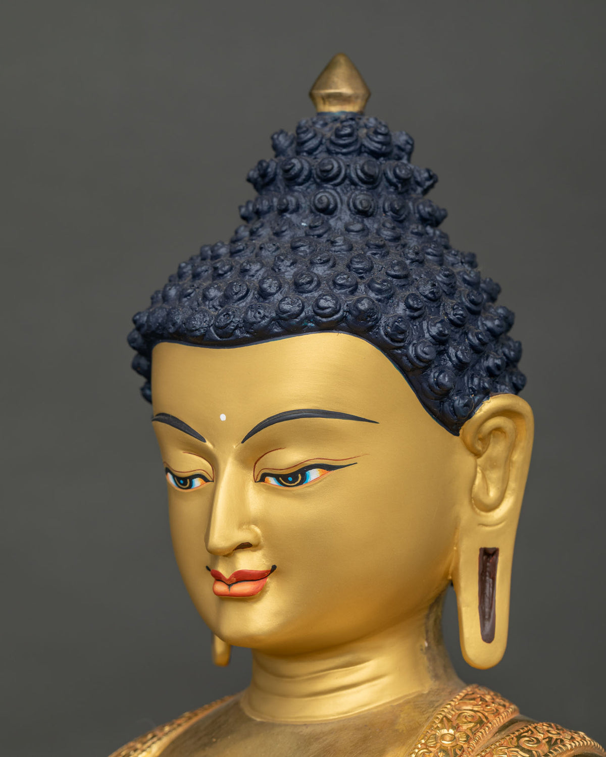 Angled close-up of Buddha Shakyamuni statue face with painted eyes, ushnisha and elongated ears