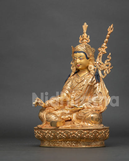 Angled side view of fire-gilded Guru Rinpoche statue holding dorje and skull cup