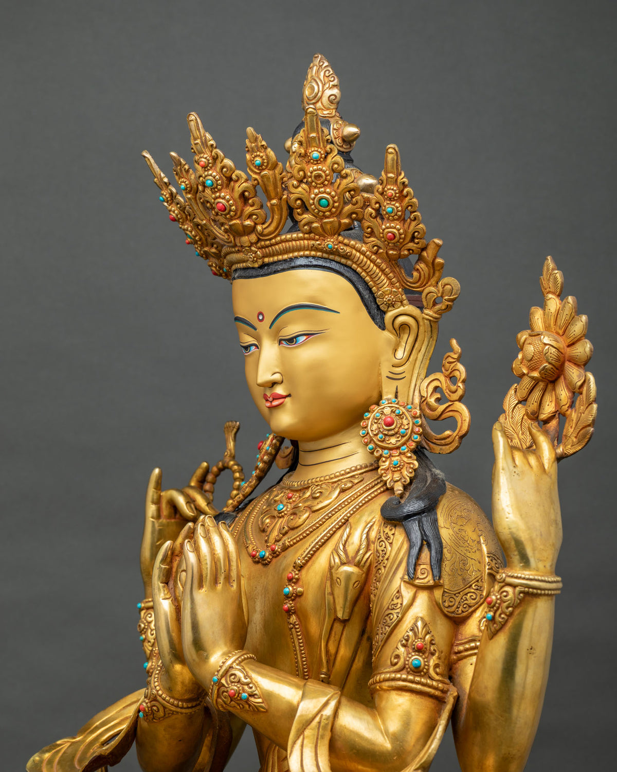 Angled view of four-armed Chenrezig statue holding crystal rosary and lotus blossom