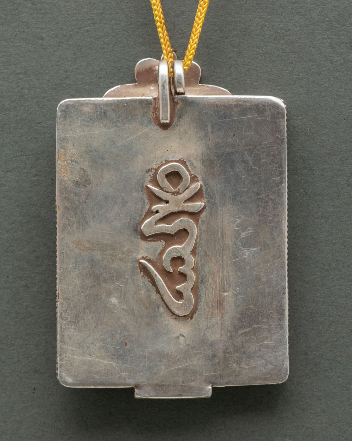 Back of Yellow Dzambhala silver Ghau locket with embossed Om seed syllable, handmade in Nepal