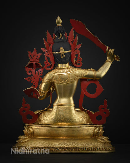 Back view of copper Manjushri statue with red painted backrest and engraved mantra letters on base