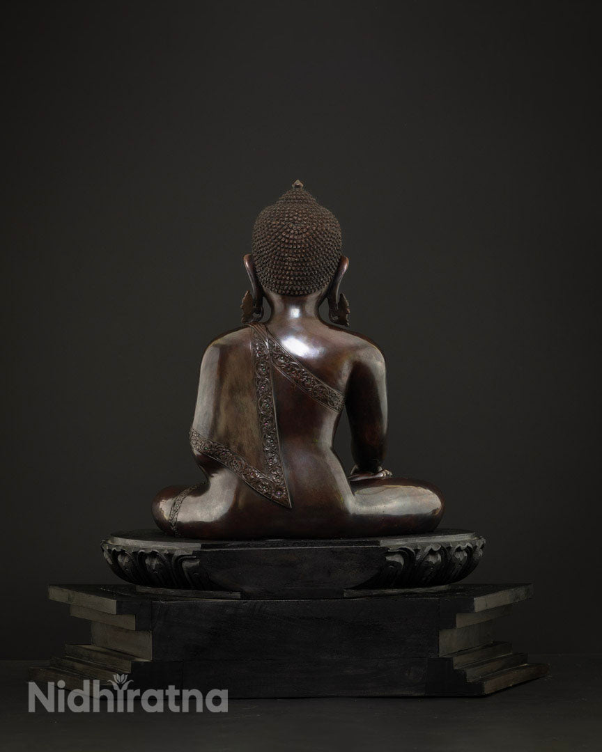 Back view of copper meditating Buddha statue showing engraved robe borders and wooden base
