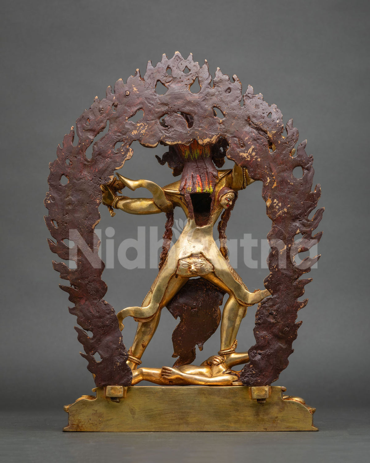 Back view of Ekajati statue showing reddish-brown flame halo backing and gold figure