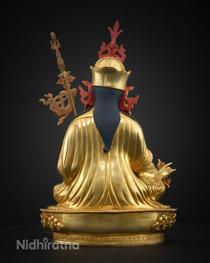 Back view of gold Guru Rinpoche statue showing draped robes, red crown ornaments, and staff