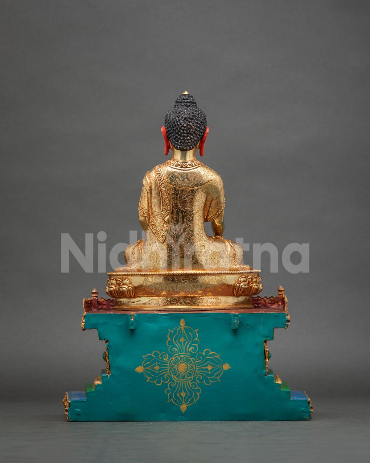 Back view of gold Shakyamuni Buddha with engraved robe and turquoise base featuring gold vajra motif