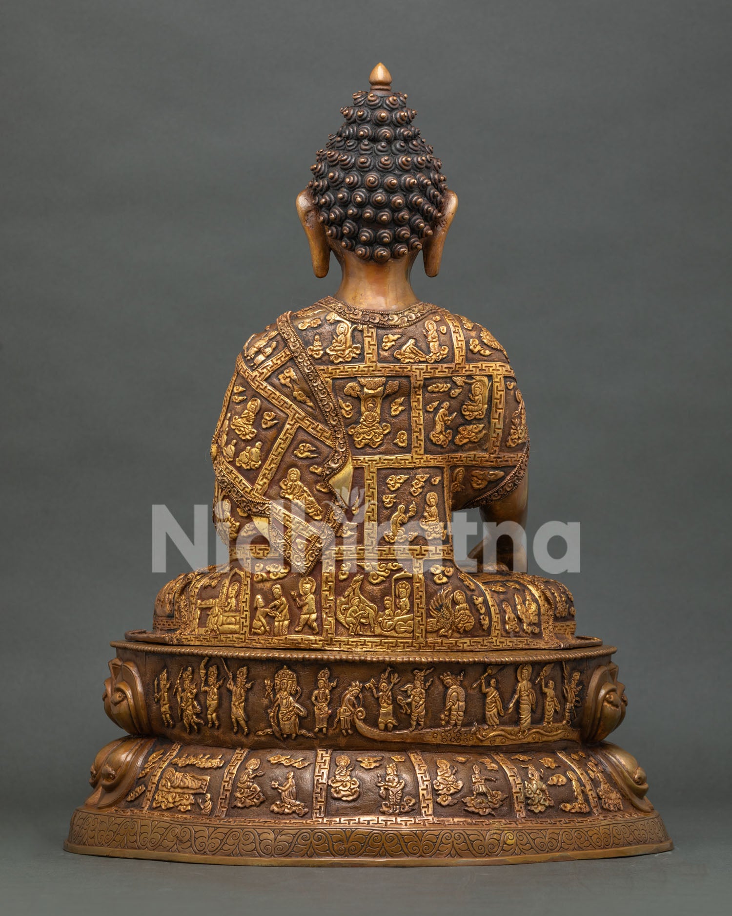 Back view of Shakyamuni Buddha statue featuring intricate gilded robe panels with sacred Buddhist story carvings