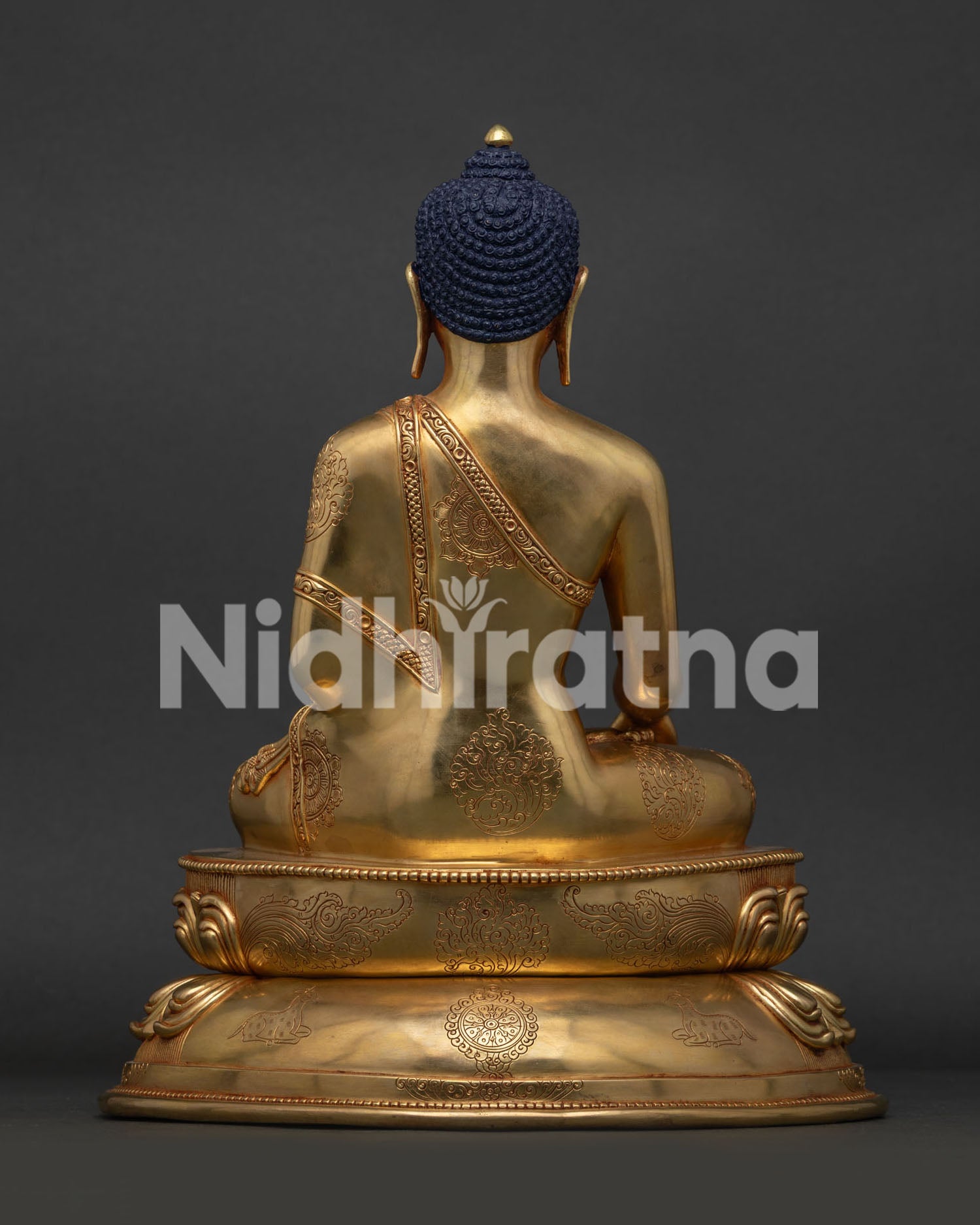 Back view of Shakyamuni Buddha statue showing wisdom wheel and deer engraved on lotus base.