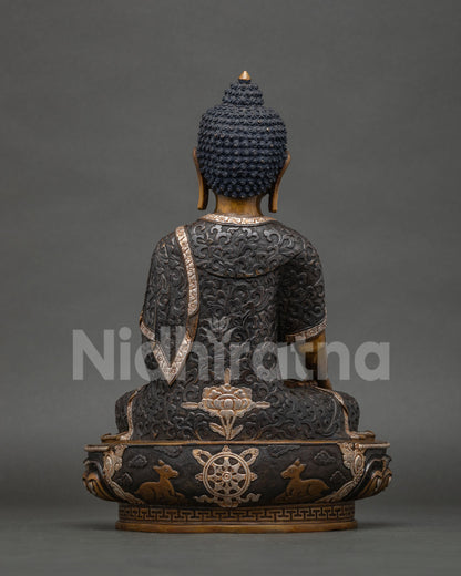 Back view of Shakyamuni Buddha statue with silver-plated floral robe, dharma wheel and deer on lotus base