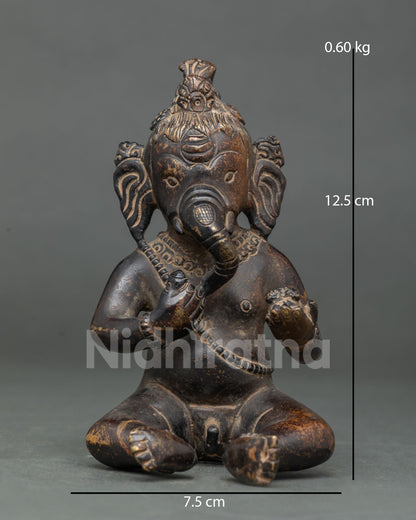 Bal Ganesha statue seated holding sweets, oxidized copper Buddhist artwork from Nepal, front view