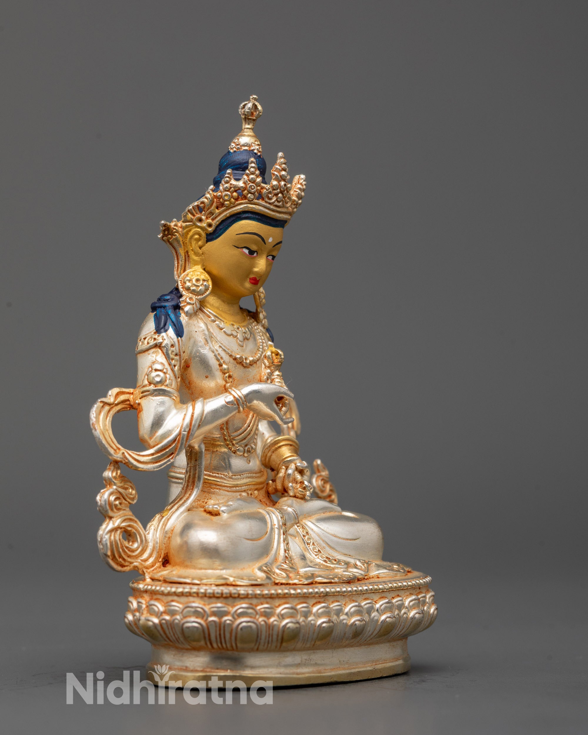 Side view of silver-plated Vajrasattva seated on a lotus base holding Dorje and Ghanta