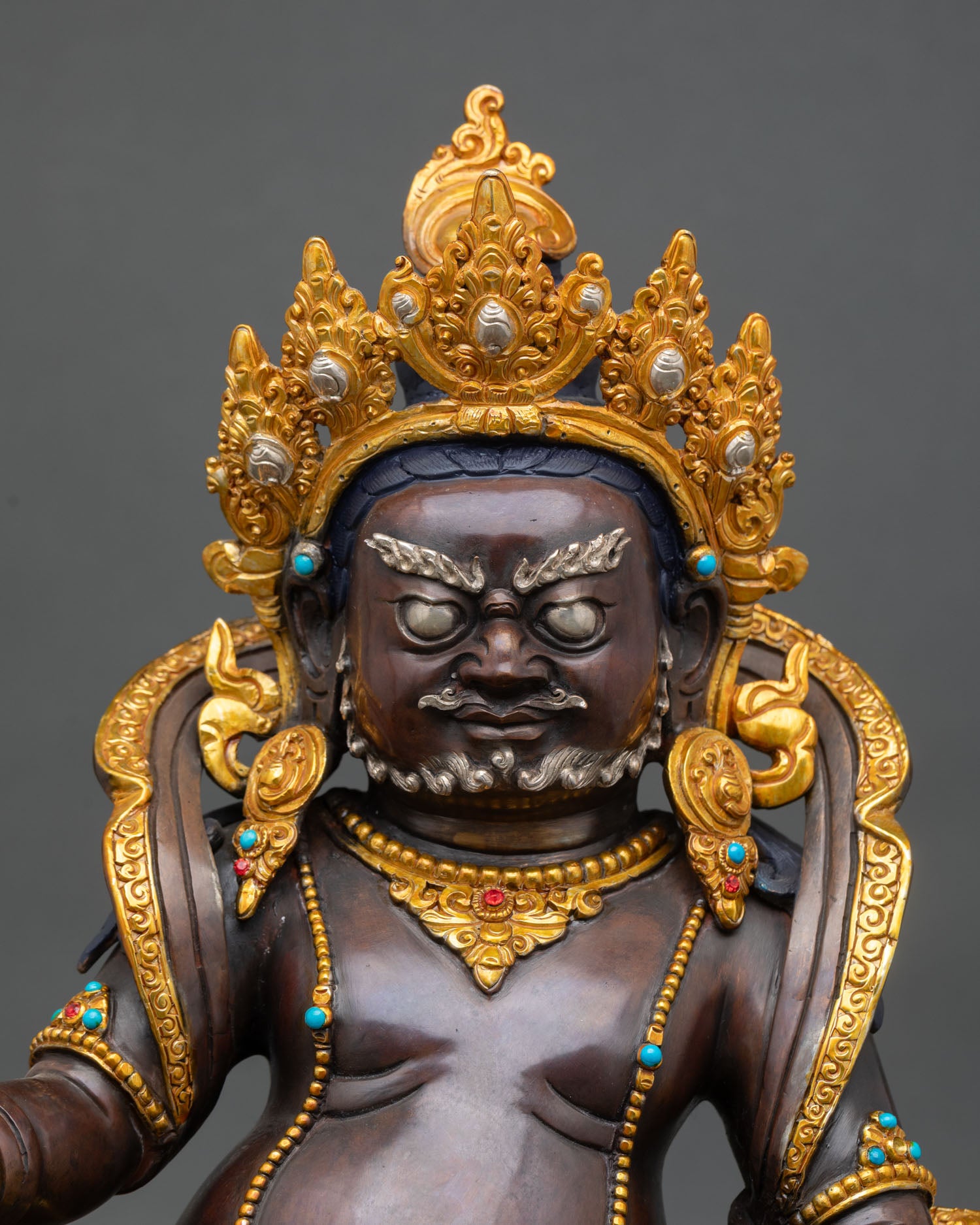 Close up Dzambhala statue face serene expression gold gilded features Tibetan wealth god