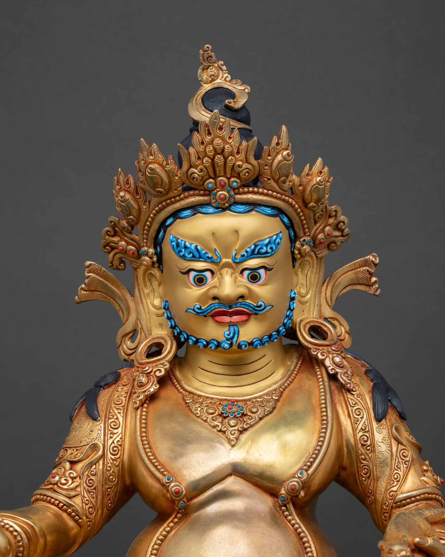 Close up Dzambhala statue gold painted face semi precious stone detailing lost wax casting Himalayan Buddhist wealth deity sculpture