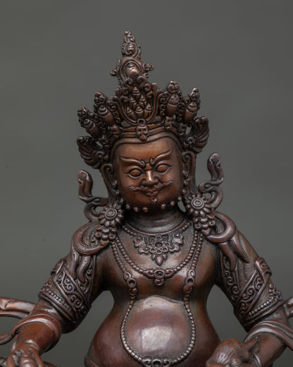 Close up Dzambhala statue showing five-jewel crown and hand-carved floral motifs.