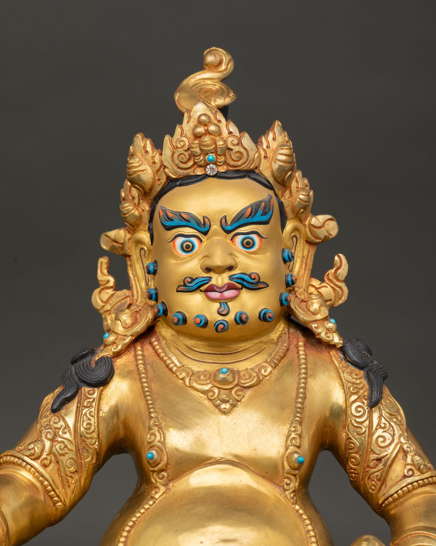 Close up face of Dzambhala statue with gold painted features, jeweled crown, and intricate Himalayan Buddhist craftsmanship