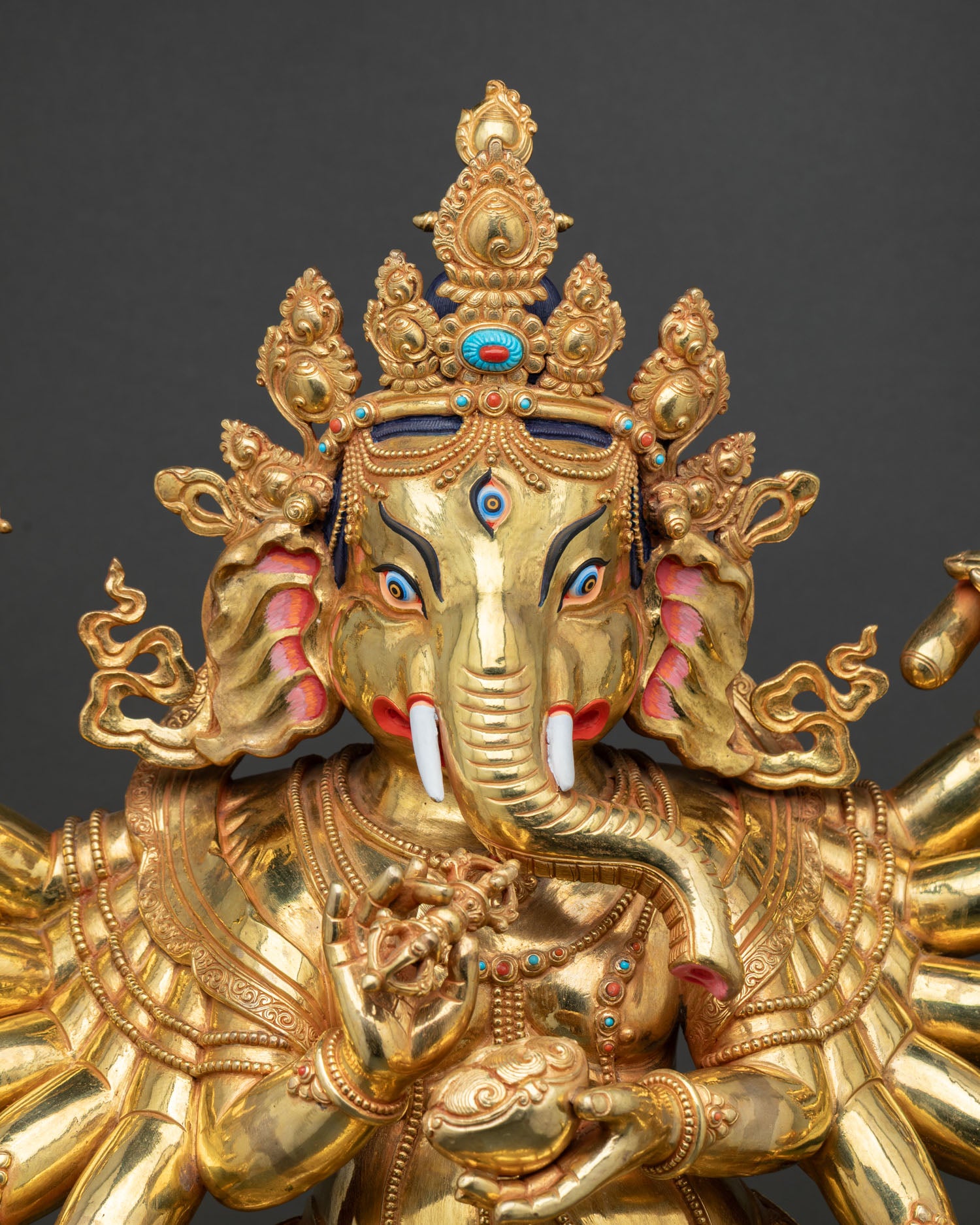 Close-up gold Ganesh statue face with ornate crown and third eye detail