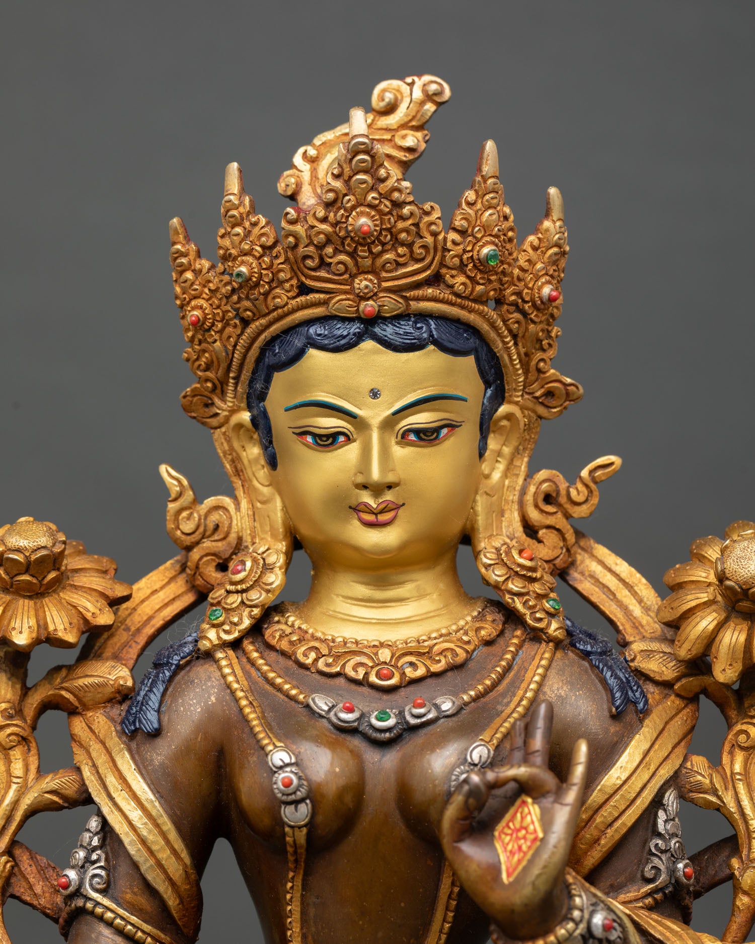 Close up Green Tara face gold painted detailing five jewel crown semi precious stones Himalayan artisan Buddhist deity sculpture detail