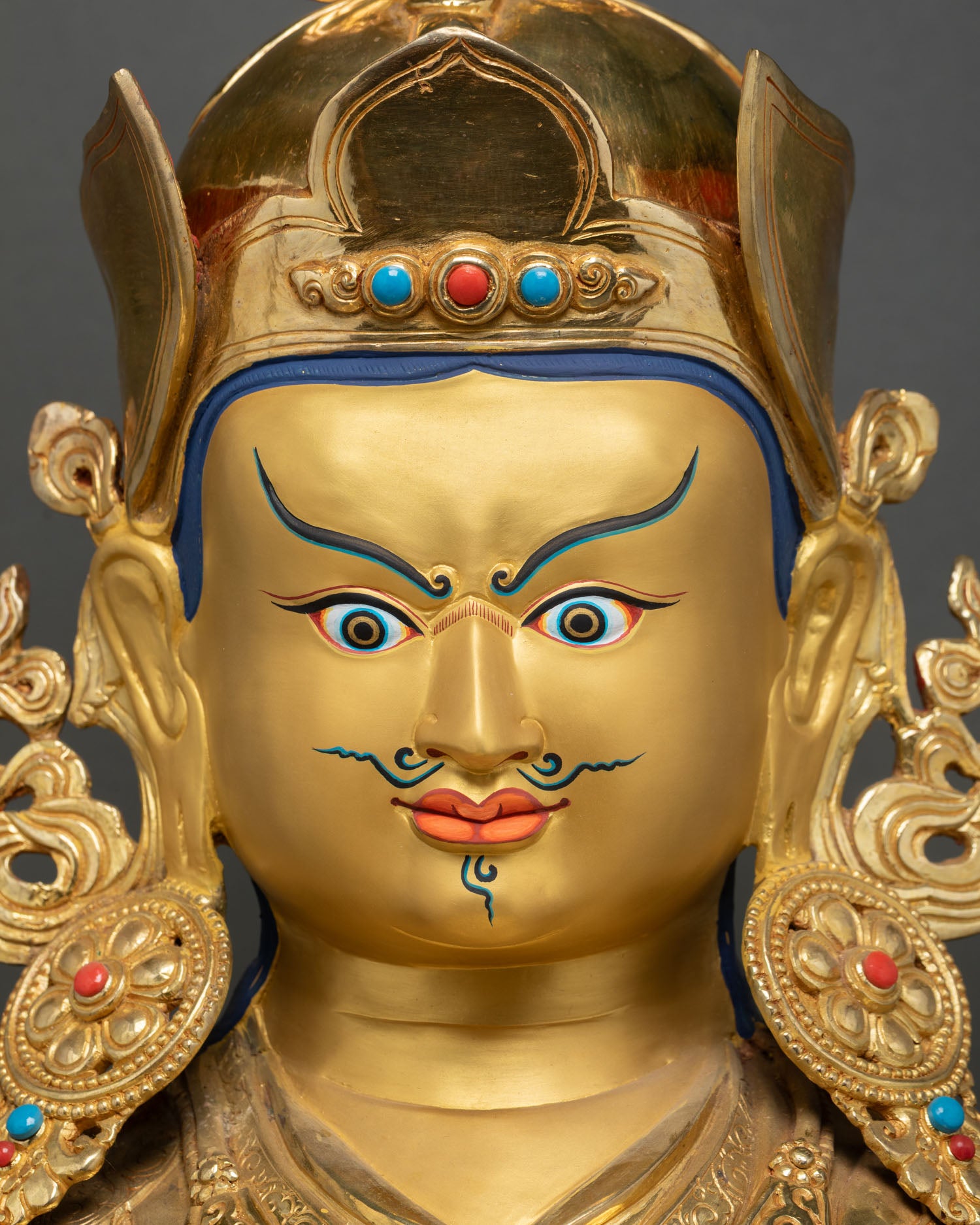 Close up Guru Rinpoche face showing semi-wrathful expression, piercing eye and traditional Tibetan Buddhist details