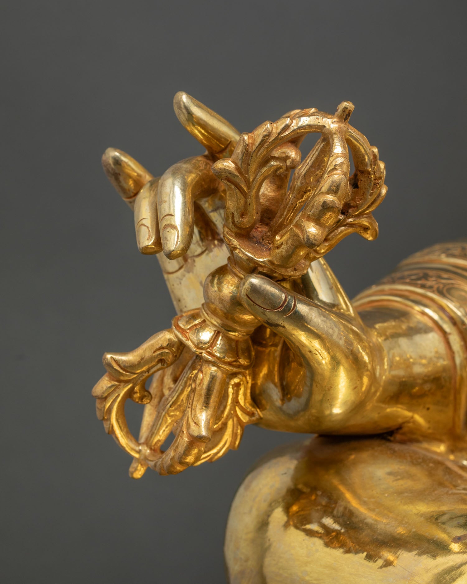 Close up Guru Rinpoche hand holding vajra with fine gold gilded Buddhist statue details