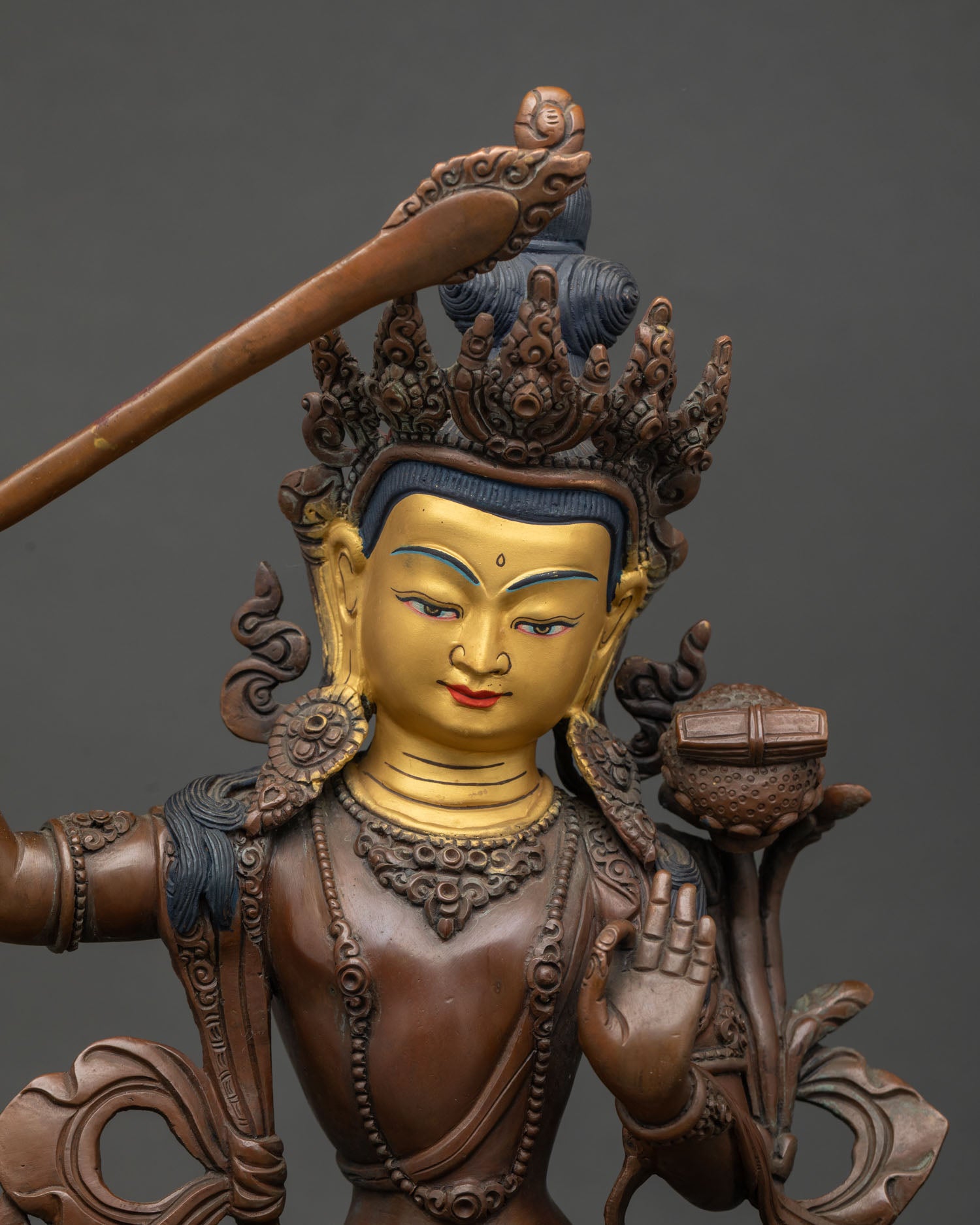 Close up Manjushri statue face with 24k gold painted finish and ornate details.