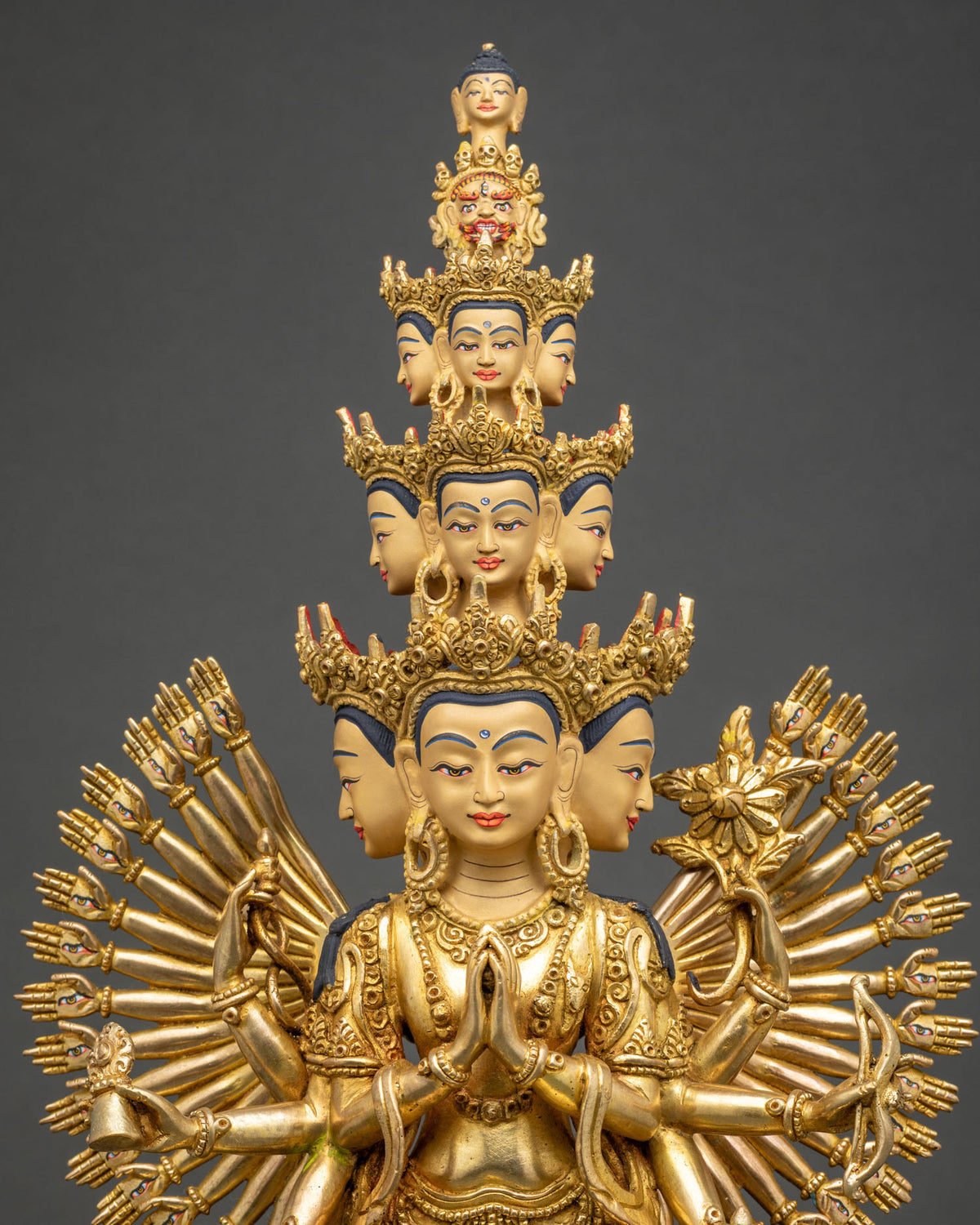 Close up of 1000 Arm Chenrezig statue showing 11 crowned heads and eye-marked palms, gilded copper