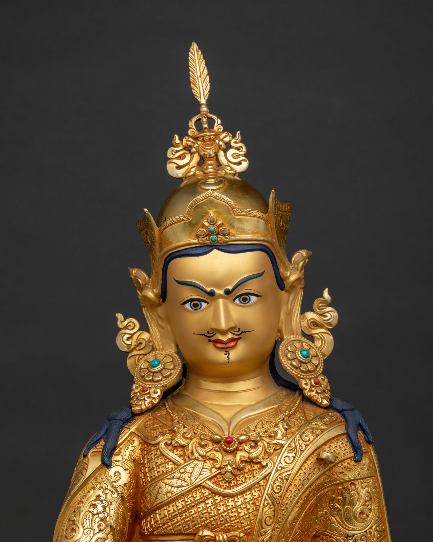 Close up of 24K gold-gilded Padmasambhava sculpture showing intricate incised robes and vajra.