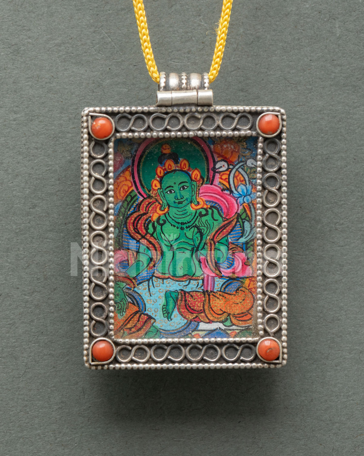 Close-up of a handcrafted Green Tara locket showcasing delicate silver filigree semi-precious coral stones and traditional Newari craftsmanship from Nepal.