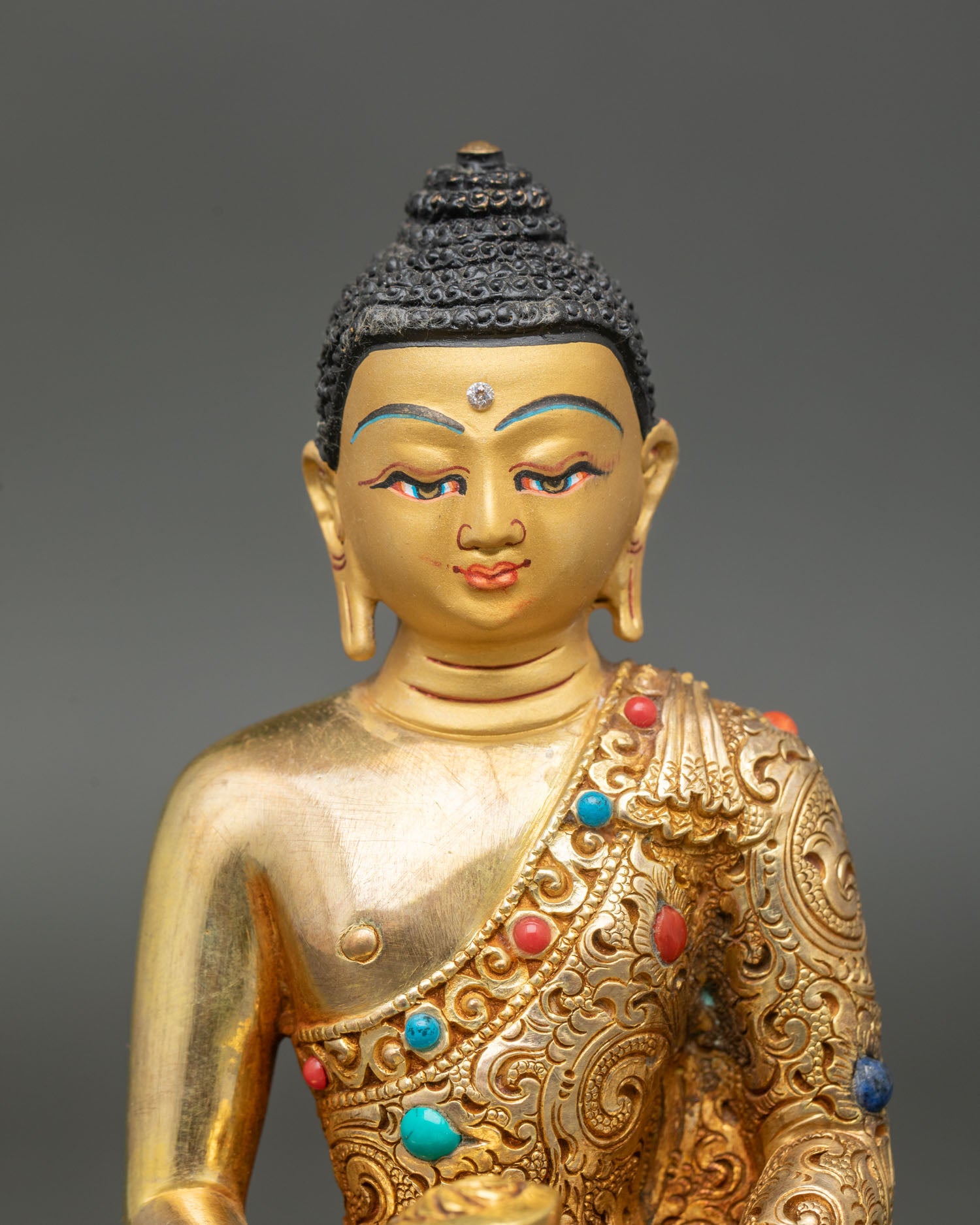 Close up of Amitabha Buddha’s gold-painted face, featuring vajra, turquoise, and coral stones.