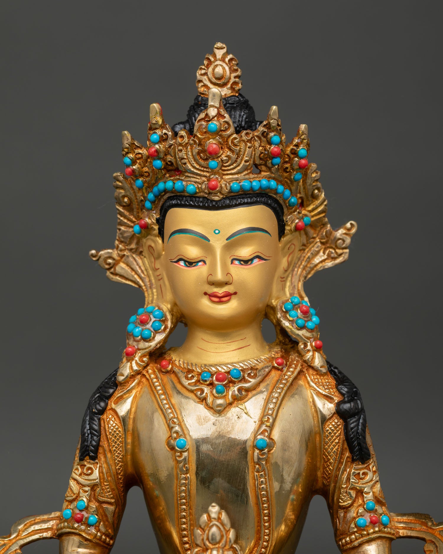 Close up of Amitayus Buddha face with gold painted details and turquoise coral stones.