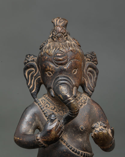 Close-up of Bal Ganesha face with long ears, curling trunk and detailed ornaments on copper statue