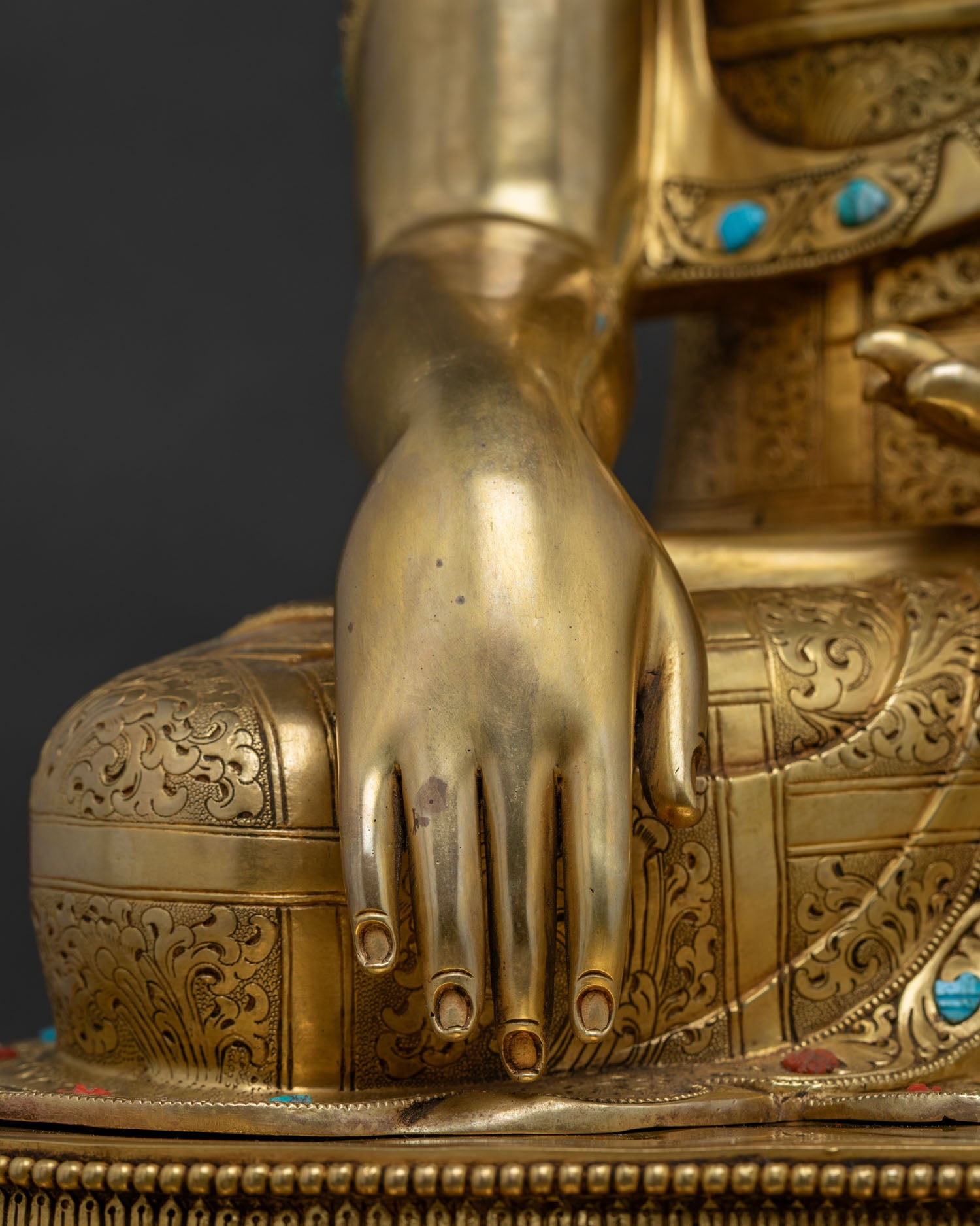 Close-up of Buddha statue's gilded arm and hand with coral and turquoise stones