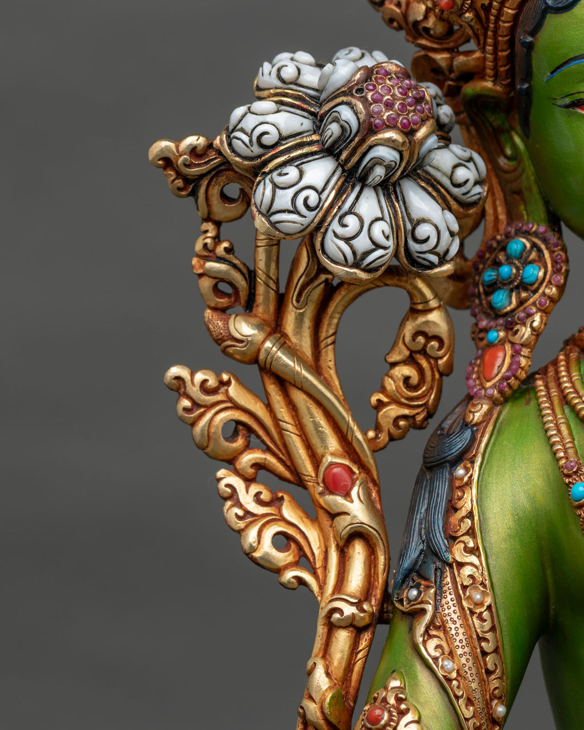 Close-up of carved white lotus flower on gilded stem of Green Tara statue with gemstone center