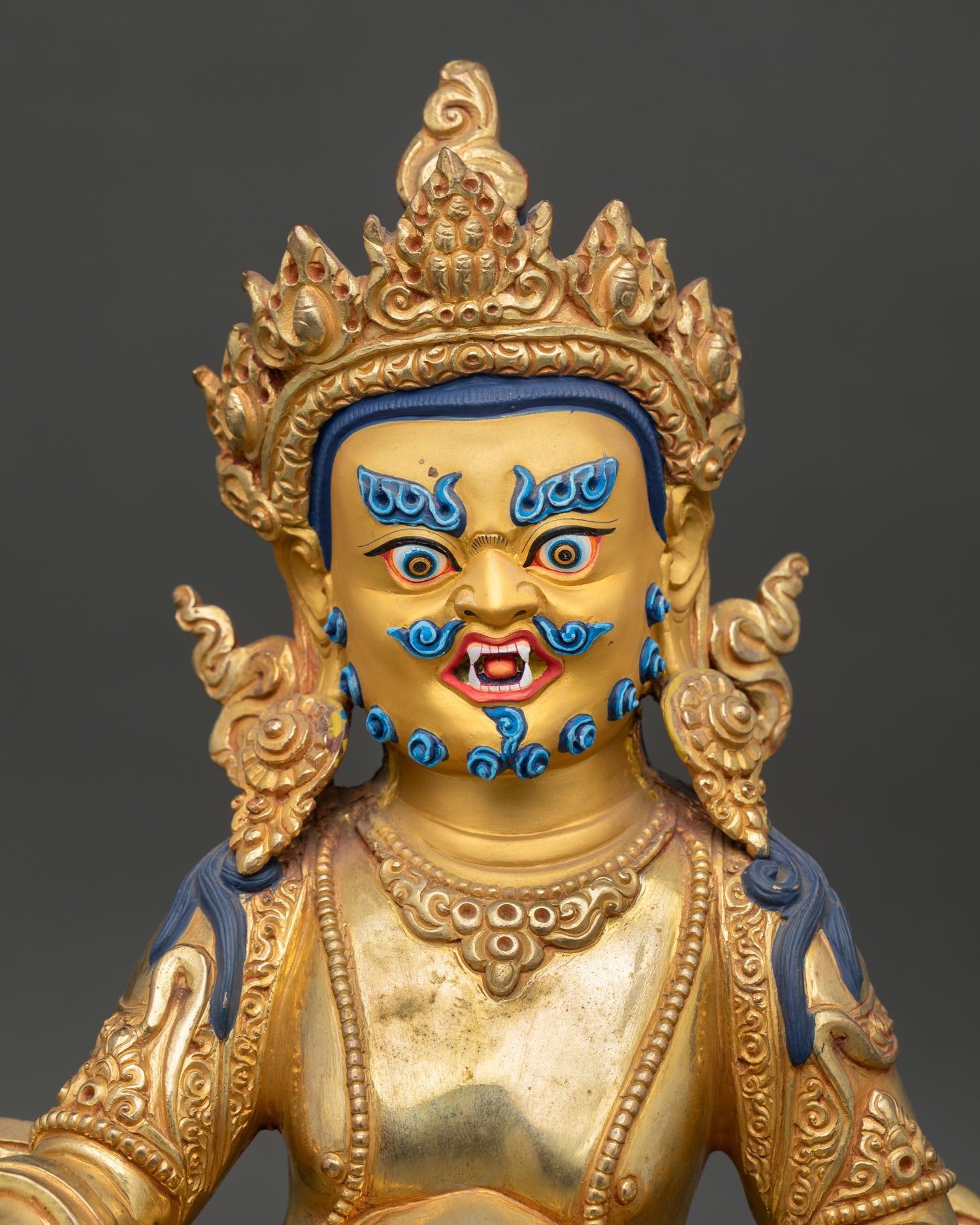 Close up of Dzambhala gold painted face, showing fierce compassionate expression and details
