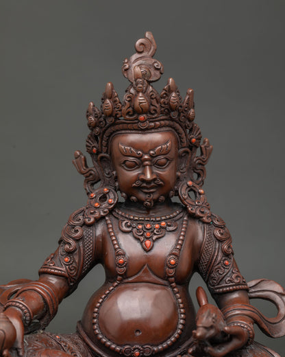 Close up of dzambhala statue showing flowing robes elaborate ornaments and detailed coral stone inlays.