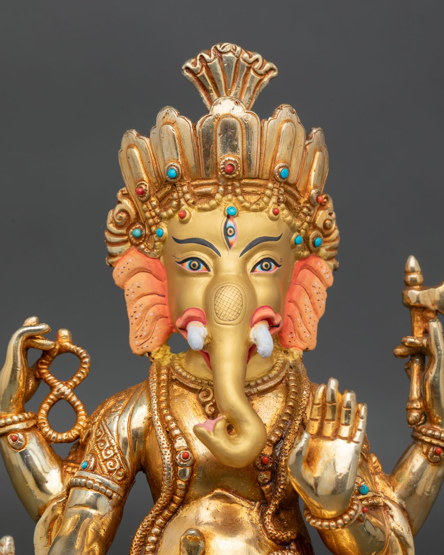 close up of four armed ganesha statue with gold gilding and sacred jewelry
