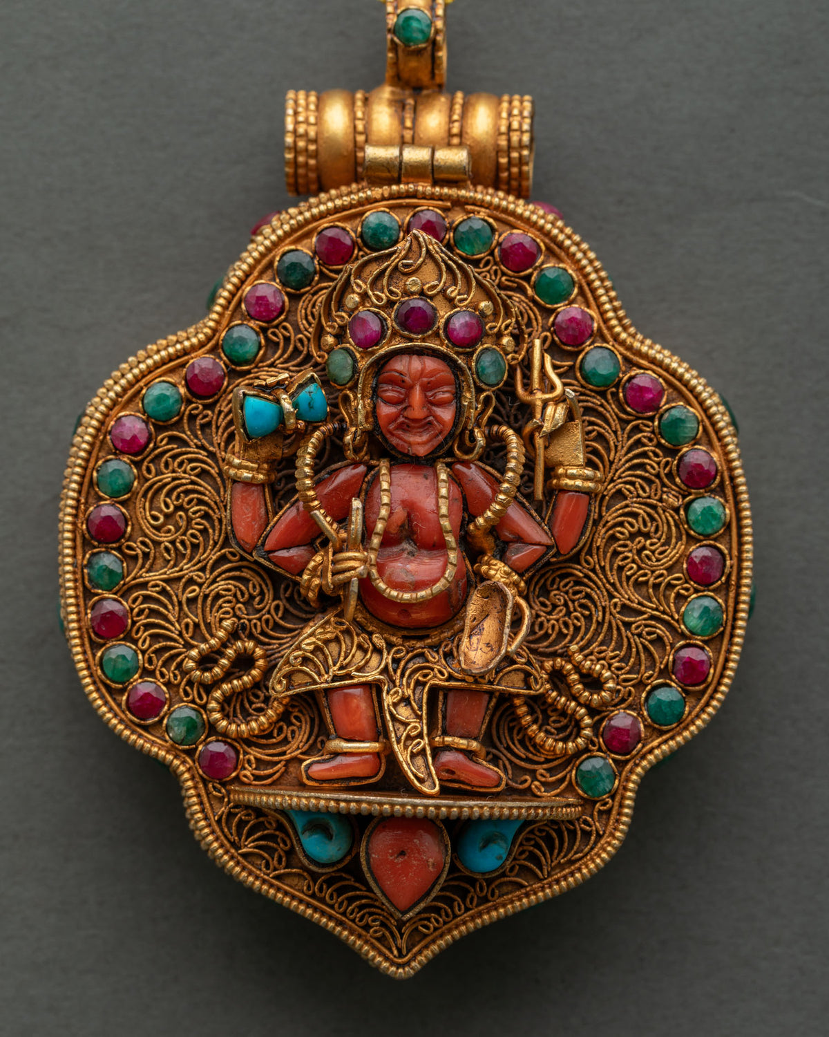 Close-up of four-armed Mahakala coral carving on gold filigree Ghau Mala with ruby and emerald