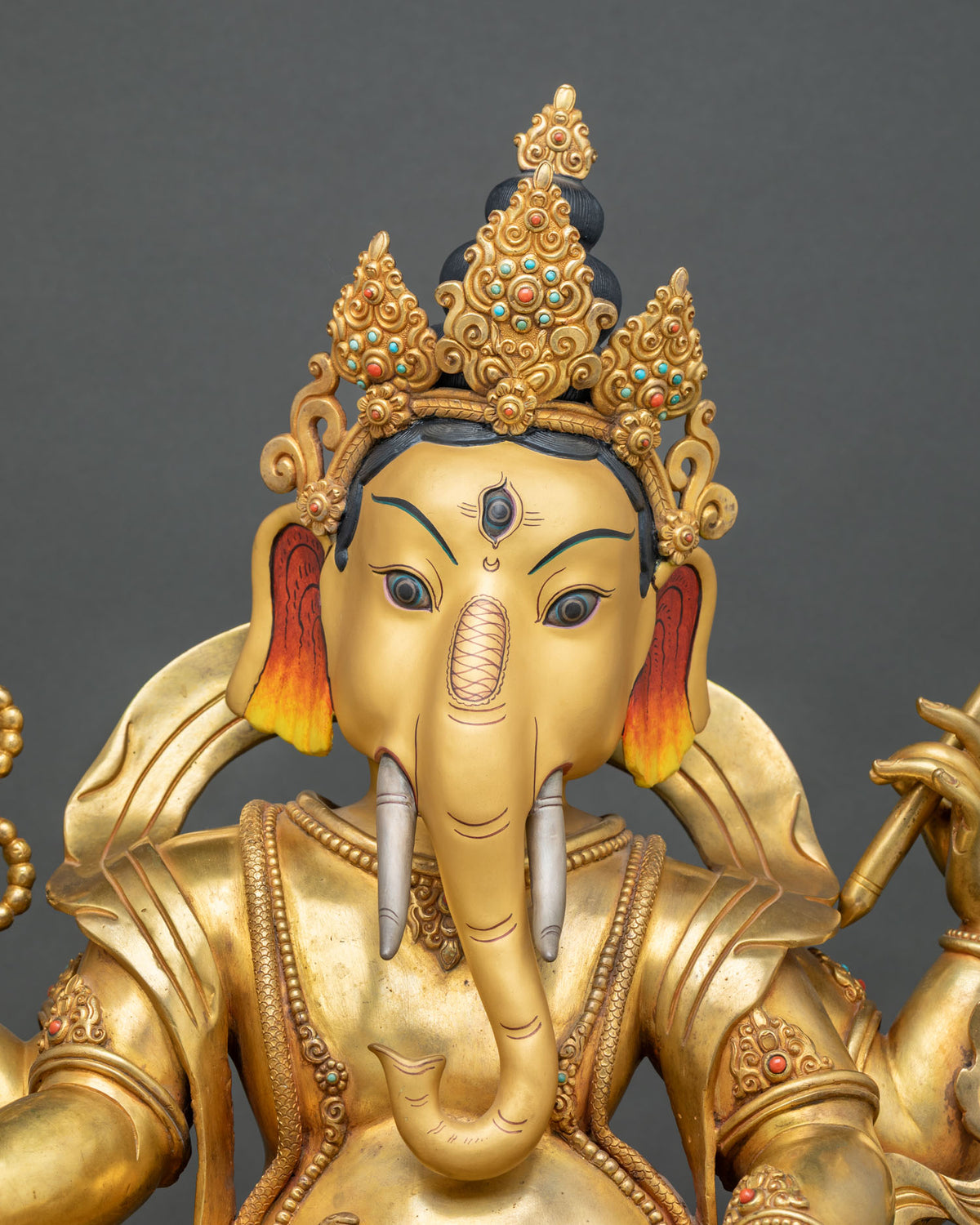 Close-up of Ganesh face with third eye, silver tusks and crown set with turquoise and coral stones