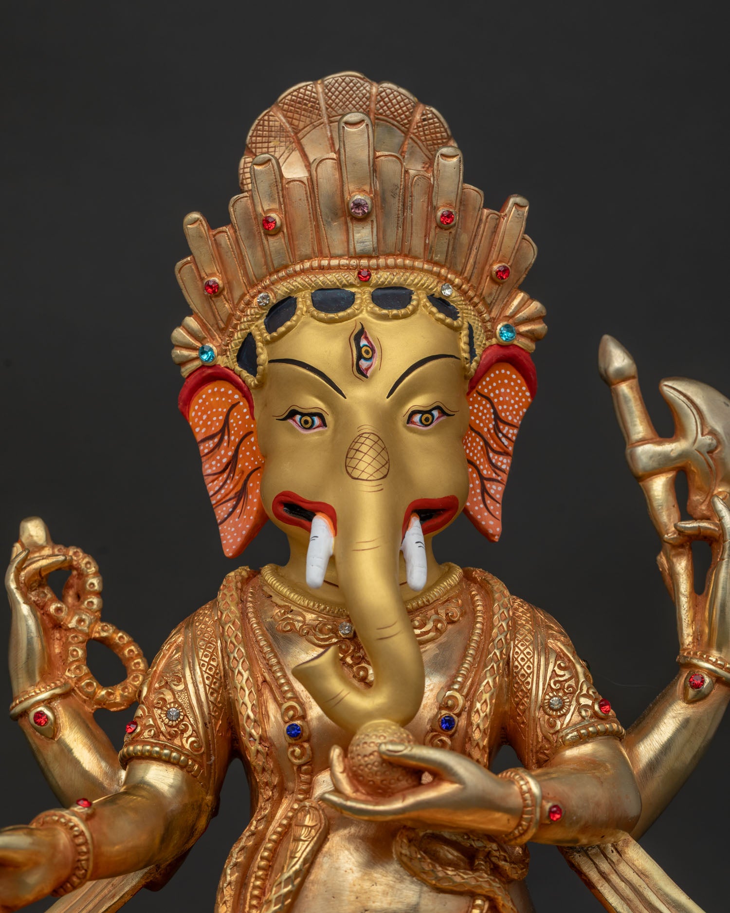 Close-up of Ganesh statue showing gold-painted face and jeweled crown details