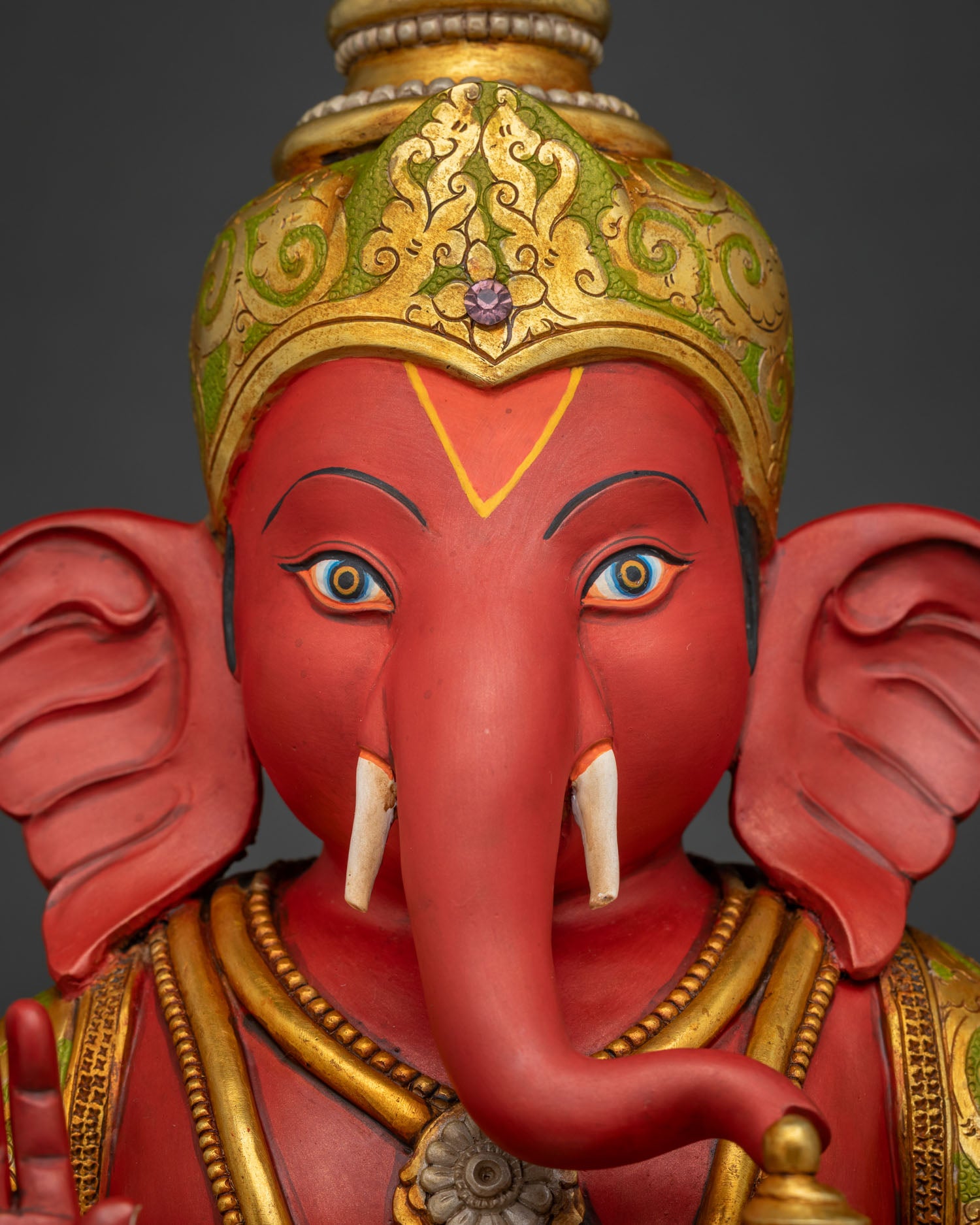 Close-up of Ganesha statue face showing gold crown and painted tilak, Nepal art