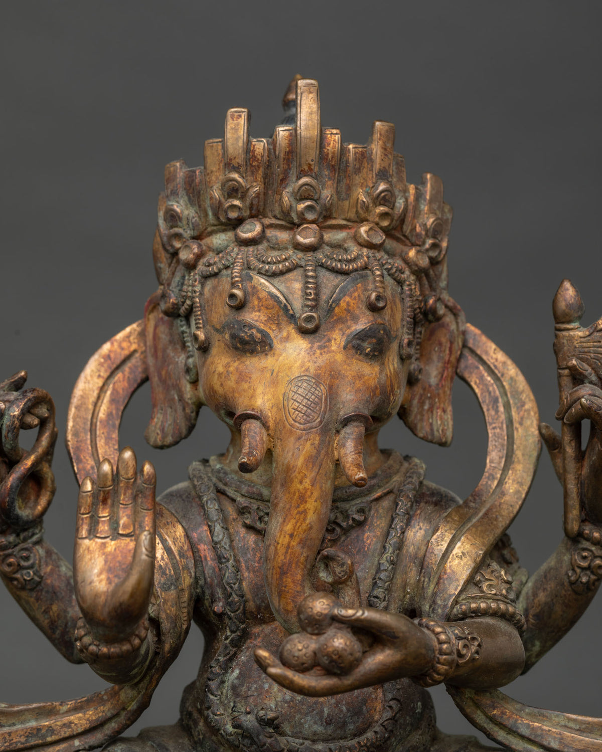 Close-up of Ganesha’s ornamented crown, trunk, and sweets offering in oxidized copper Ganpati statue