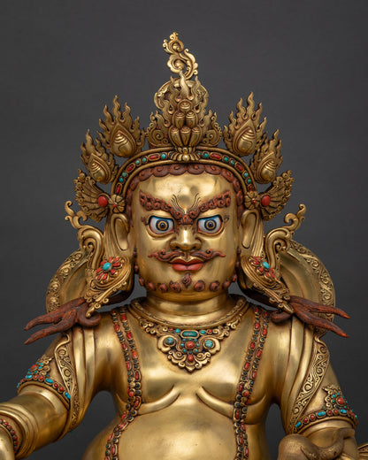 Close-up of gold Dzambhala statue showing hand-chased ornaments and gemstone inlays.