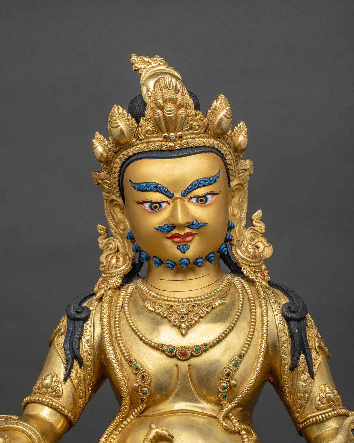 Close up of gold fire-gilded Dzambhala copper statue with turquoise and coral stones
