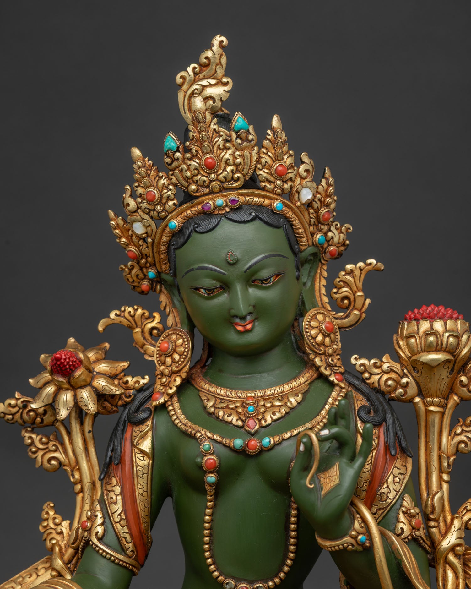 Close-up of gold gilded Green Tara statue seated on lotus throne for meditation.