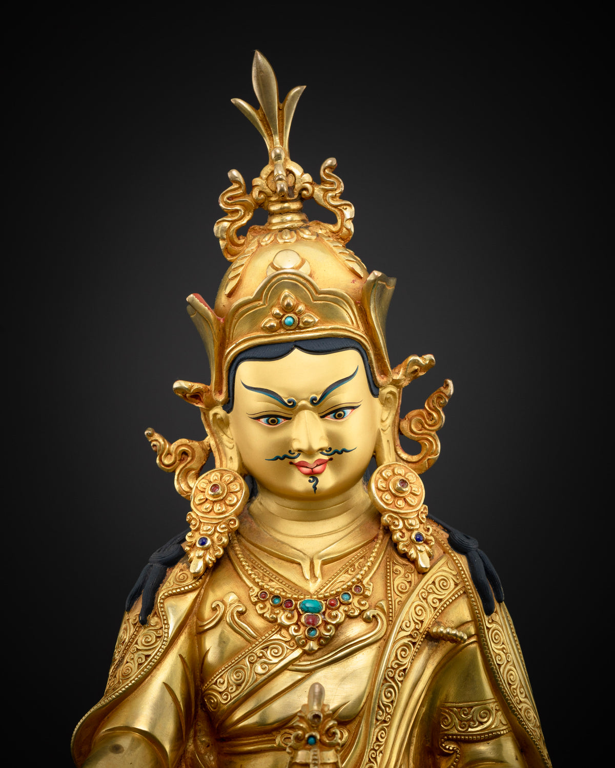 Close-up of gold-gilded Guru Rinpoche statue face with painted eyes, mustache, and gemstone necklace